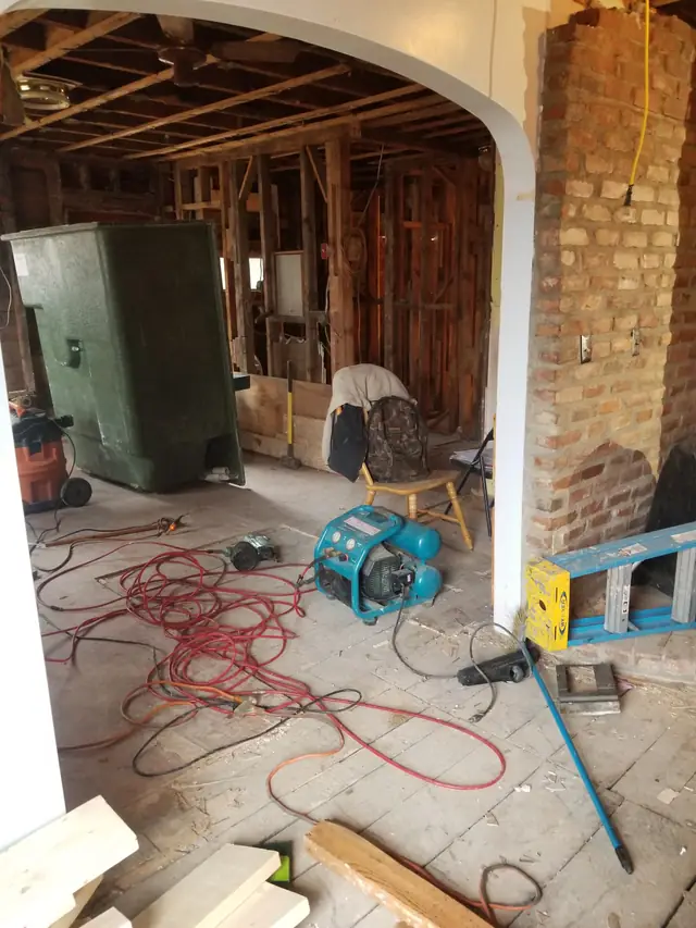 Room opened to the studs beside a brick pier, cords and a saw on the subfloor