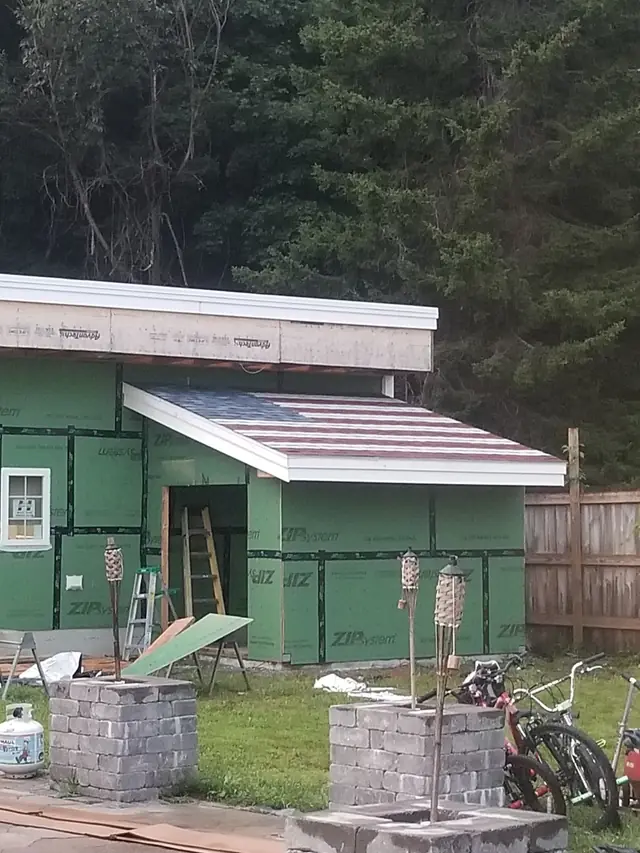 Addition framed in green sheathing under a new shed roof, set on stone piers