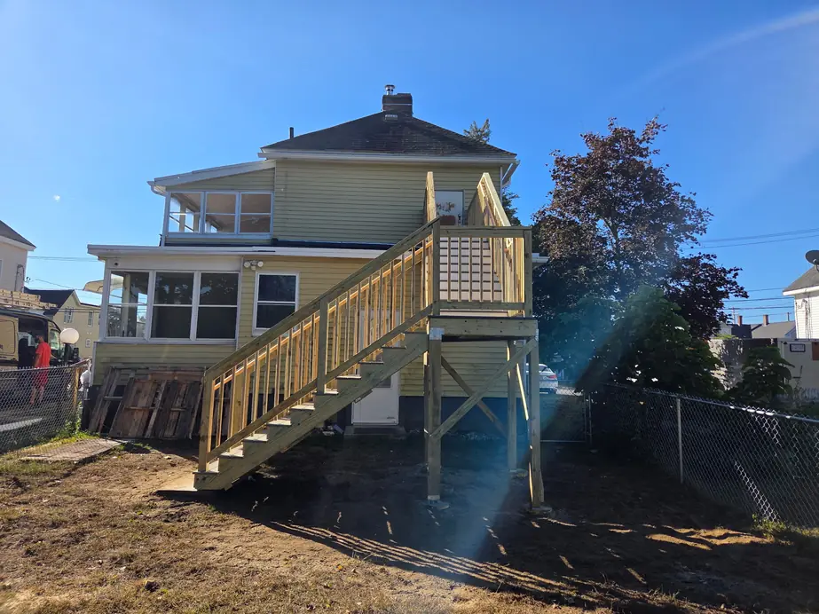 Elevated pressure-treated deck and stair at the rear of a yellow two-family house