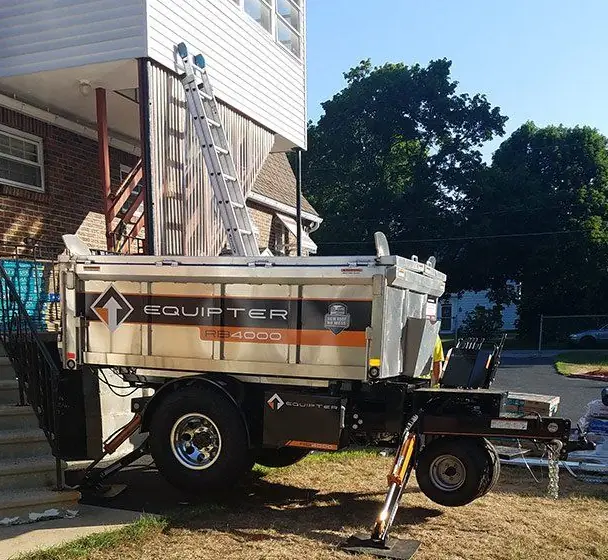 Equipter roof-loading trailer parked under a ladder at a two-storey house